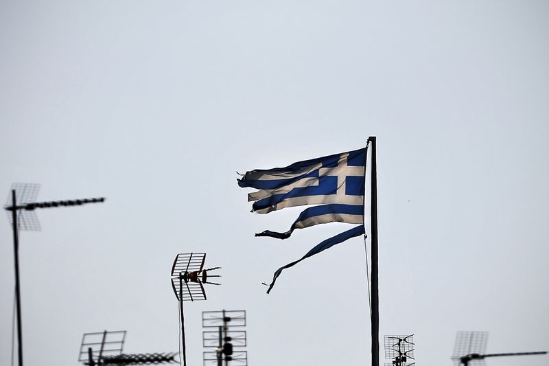 © Reuters. A tourist makes her way past a Greek national flag and an EU flag on the islet of Saint George, part of the municipality of Kastellorizo, Greece's easternmost island