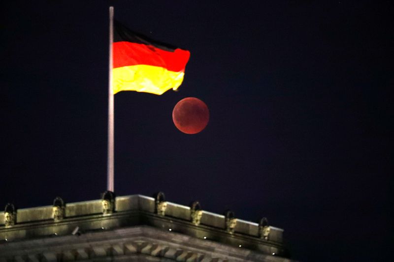 &copy; Reuters. La luna durante un'eclissi lunare accanto alla bandiera tedesca in cima al palazzo del Reichstag a Berlino, Germania, 27 luglio 2018. REUTERS / Fabrizio Bensch