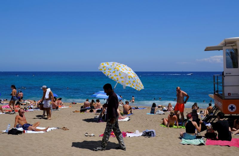 © Reuters. A seller renting a sun umbrella for beachgoers walks at a beach in Barcelona, amid the coronavirus disease (COVID-19) pandemic, Spain July 14, 2021. REUTERS/Nacho Doce