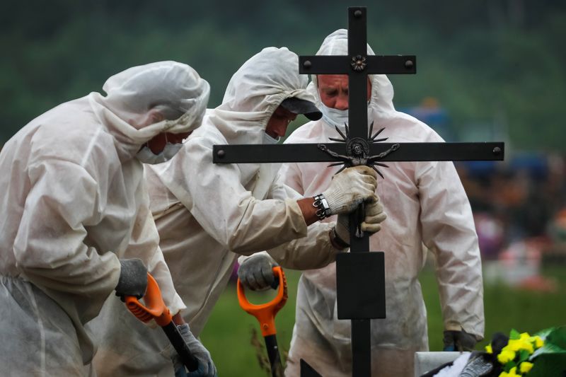 © Reuters. Grave diggers wering personal protective equipment (PPE) bury a person, who presumably died of the coronavirus disease (COVID-19) in the special purpose section of a graveyard on the outskirts of Saint Petersburg, Russia June 10, 2020.  REUTERS/Anton Vaganov
