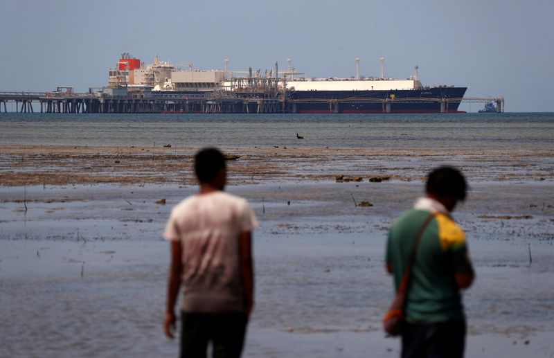&copy; Reuters. FILE PHOTO: Locals walk along a small beach where a Liquefied Natural Gas (LNG) carrier called Kumul is docked at the marine facility of the ExxonMobil PNG Limited operated LNG plant at Caution Bay, located on the outskirts of Port Moresby in Papua New Gu