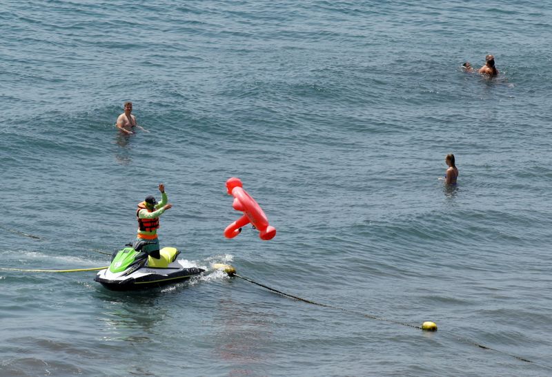 &copy; Reuters. Un hombre en una moto de agua libera un flotador con forma de flamenco de una red junto a unos turistas en la isla de Gran Canaria, Islas Canarias, España, el 19 de julio de 2021. REUTERS/Borja Suárez