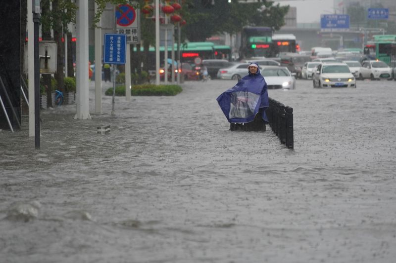 &copy; Reuters. أحد السكان يرتدي غطاء واقيا من الأمطار في شارع غمرته مياه الفيضانات في إقليم خنان بوسط الصين يوم الثلاثاء. صورة لرويترز.