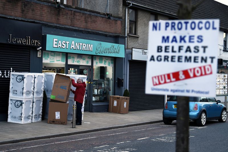 &copy; Reuters. FILE PHOTO: A man sorts through a delivery of washing machines with a sign is seen across the road featuring a message against the Brexit border checks in relation to the Northern Ireland protocol in the town centre of Larne, Northern Ireland. February 12