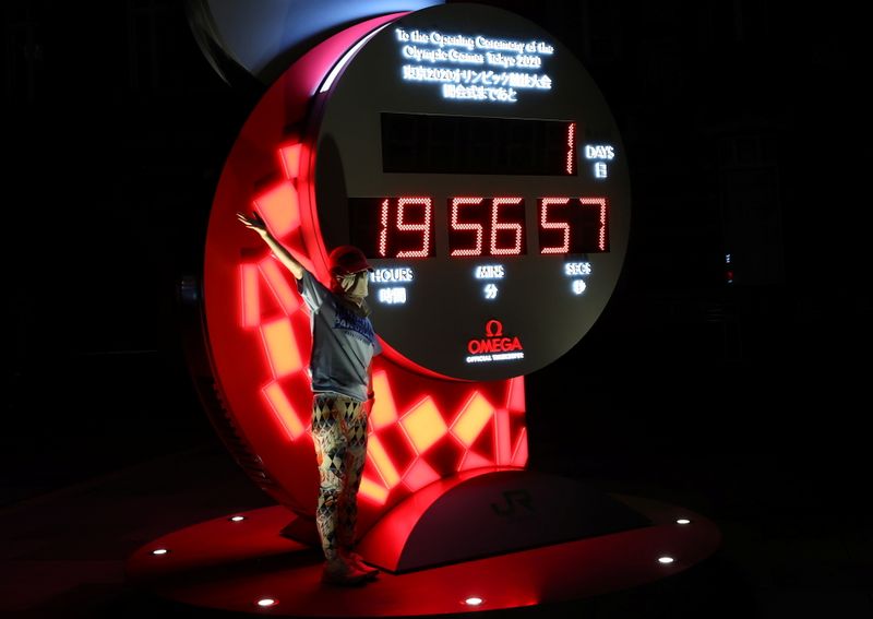 &copy; Reuters. امرأة تضع كمامة للوقاية من فيروس كورونا تقف لالتقاط صورة أمام شاشة للعد التنازلي لحفل افتتاح أولمبياد طوكيو 2020 في العاصمة اليابانية يوم الخ