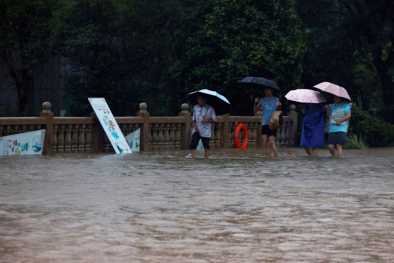 &copy; Reuters. People holding umbrellas amid heavy rainfall wade through floodwaters on a bridge in Hebi, Henan province, China July 22, 2021. REUTERS/Aly Song