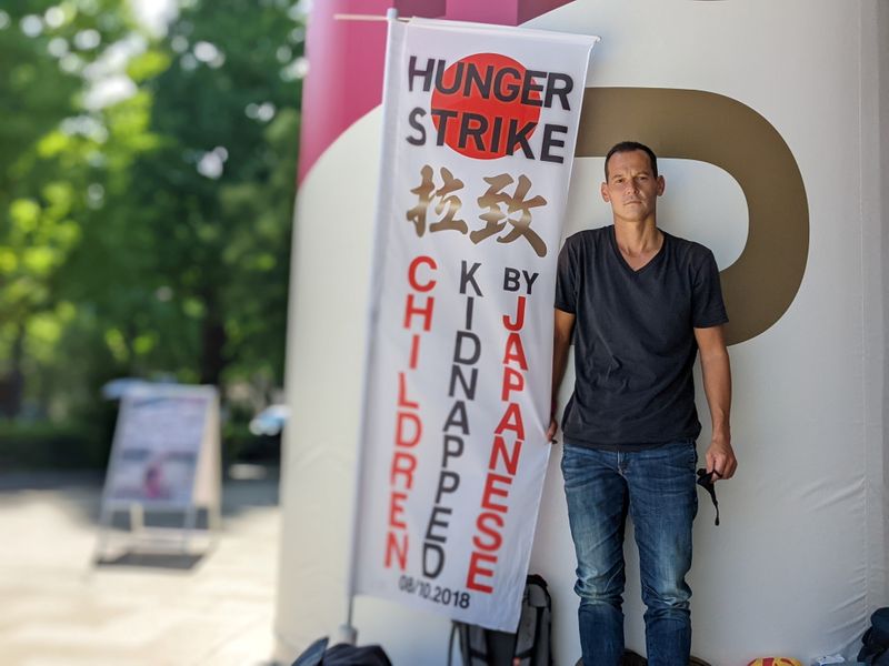 &copy; Reuters. French father-of-two Vincent Fichot stands with his banner where he has been on a hunger strike since July 10 to protest what he says is Japan's sanctioning of child 'abductions' by a parent, near the Olympic Stadium in Tokyo, Japan July 21, 2021. REUTERS