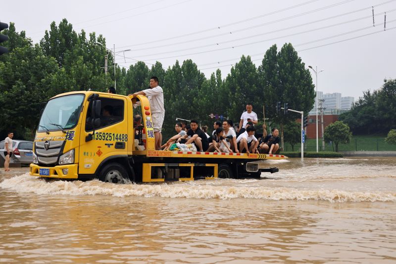 © Reuters. People ride on the back of a truck as they make their way through floodwaters following heavy rainfall in Zhengzhou, Henan province, China July 23, 2021. REUTERS/Aly Song