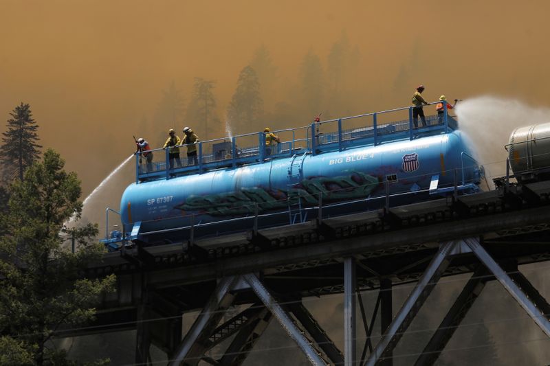 &copy; Reuters. FILE PHOTO: Firefighters spray water from a fire train to hot spots along the tracks over Rock Creek Bridge as the Dixie Fire grows in Plumas National Forest, California, U.S., July 15, 2021. REUTERS/David Swanson     