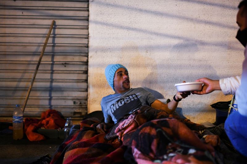 &copy; Reuters. Vinicius, un hombre sin hogar de 33 años, recibe comida de Marlon Lemos de la ONG doAcao, mientras distribuyen alimentos y cobijas a las personas sin techo en medio de una inusual ola de frío en Rio de Janeiro, Brasil. 29 de julio, 2021.   REUTERS/Lucas