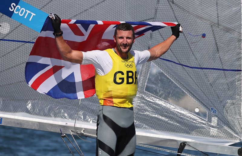 © Reuters. البريطاني جايلز سكوت يرفع علم بلاده بعد الفوز ببذهبية الشراع فئة فين للرجال بأولمبياد طوكيو يوم الثلاثاء. رويترز