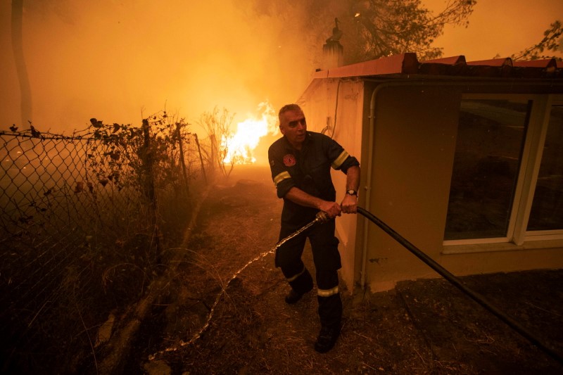 &copy; Reuters. Un bombero tira de una manguera, mientras un incendio forestal arde en el pueblo de Pefki, en la isla de Evia, Grecia, 8 de agosto de 2021. REUTERS/Nikolas Economou