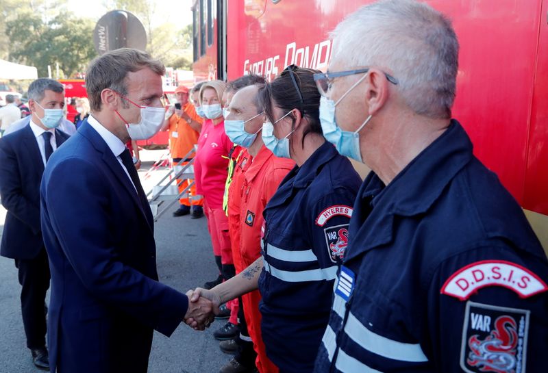 © Reuters. الرئيس الفرنسي إيمانويل ماكرون يصافح رجال الإطفاء أثناء زيارة لبلدة  سان تروبيه الساحلية في جنوب فرنسا يوم الثلاثاء. صورة لرويترز من ممثل وكالات أنباء. 