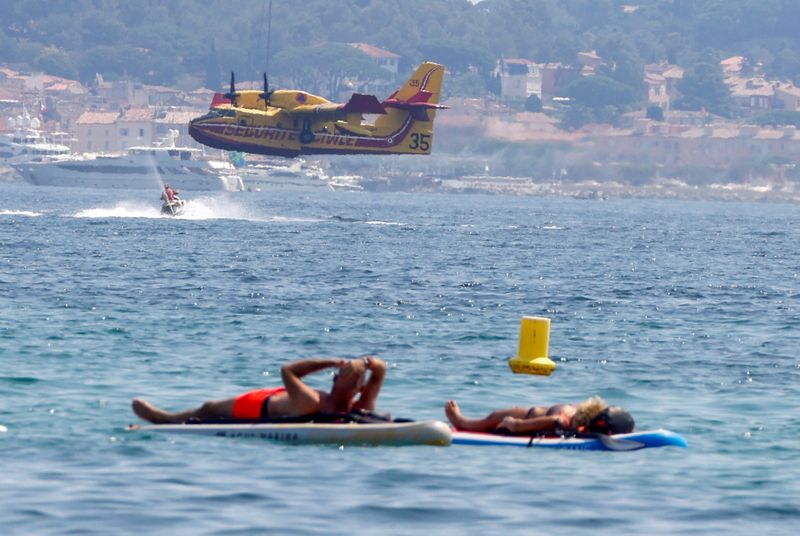 © Reuters. People float on boards as a Canadair aircraft flies after being filled up with water to help with efforts in extinguishing a major fire that broke out in the Var region, at the Gulf of Saint Tropez, France August 17, 2021. REUTERS/Eric Gaillard