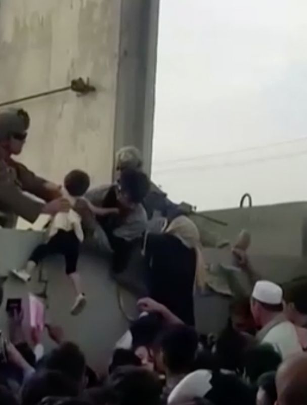 &copy; Reuters. Dans la foule qui se presse devant l'aéroport de Kaboul, une petite fille est soulevée par-dessus le mur d'enceinte et un soldat américain la prend dans ses bras. /Photo prise le 19 août 2021/REUTERS/Rise to Peace