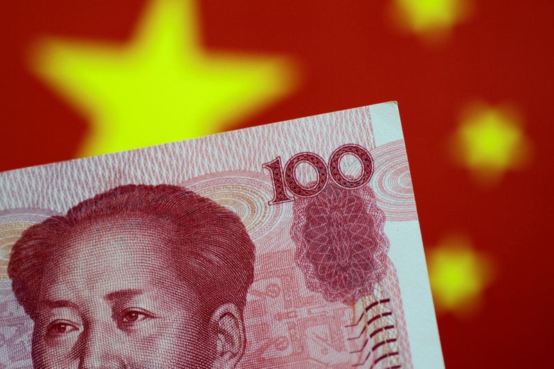 © Reuters. Una banconota da 100 yuan davanti alla bandiera cinese.     REUTERS/Thomas White