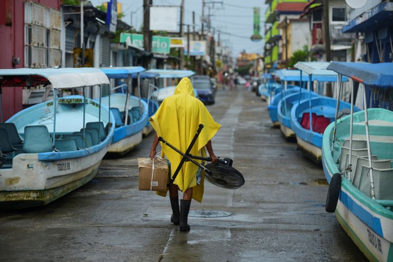 &copy; Reuters. Un hombre carga un ventilador y una caja mientras pasa junto a los barcos turísticos que fueron sacados del agua por seguridad mientras el huracán Grace cobraba más fuerza antes de llegar a tierra, en Tecolutla, México. 20 de agosto de 2021. REUTERS/O