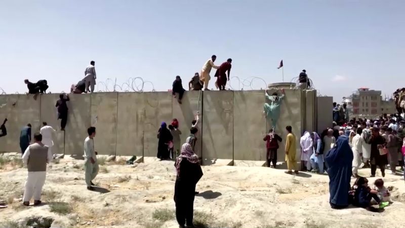 &copy; Reuters. Uomini e donne scavalcano il muro ricoperto di filo spinato per entrare all'aeroporto di Kabul. Afghanistan, 16 agosto 2021 August 16, 2021 REUTERS TV/via REUTERS