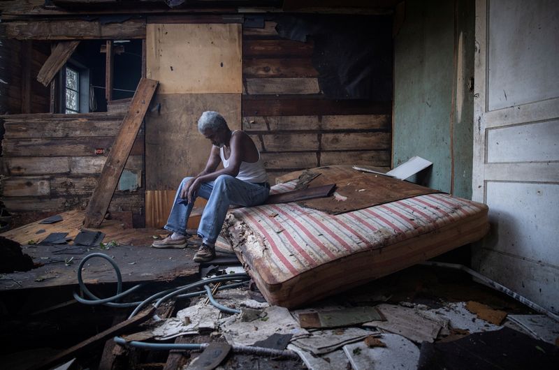 © Reuters. Theophilus Charles, 70, sits inside his house which was heavily damaged by Hurricane Ida in Houma, Louisiana, U.S., August 30, 2021. REUTERS/Adrees Latif  