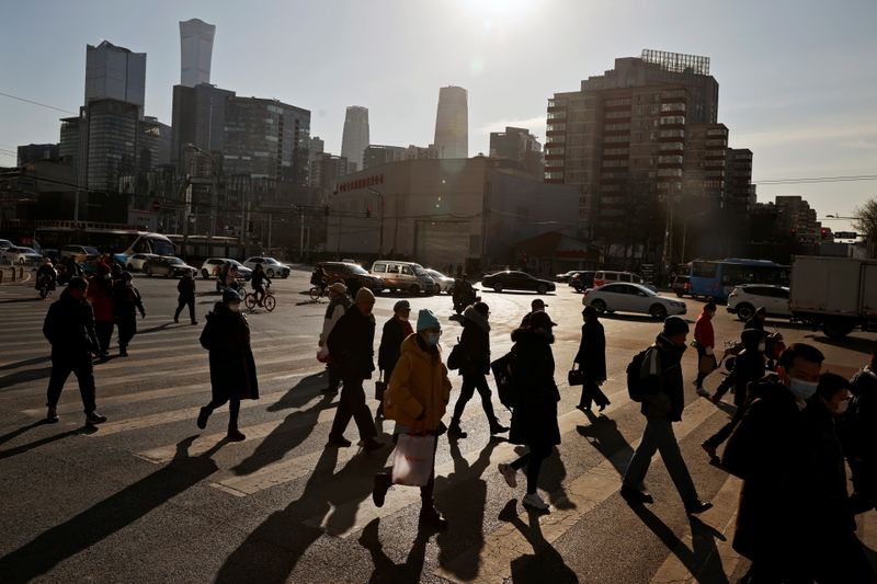 &copy; Reuters. FILE PHOTO: People cross a street during morning rush hour in front of the skyline of the central business district (CBD) in Beijing, China December 15, 2020. REUTERS/Thomas Peter