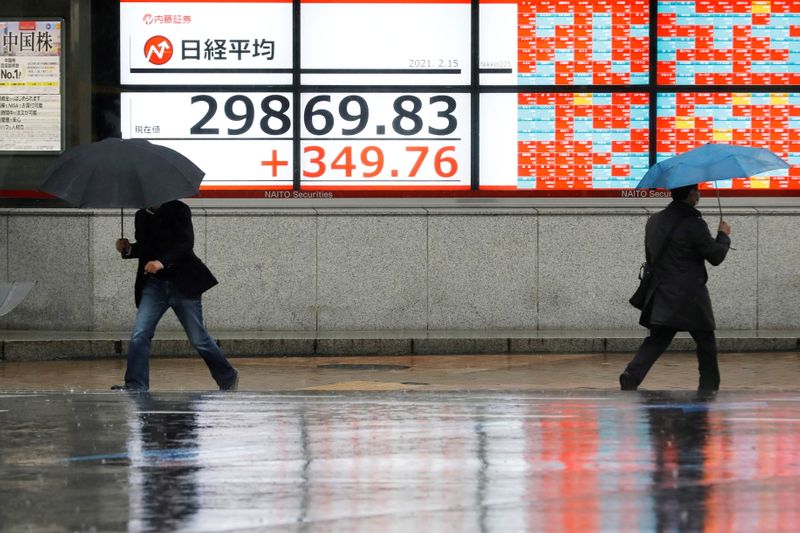 &copy; Reuters. Men holding umbrellas walk in front of an electric board showing Nikkei index at a brokerage in Tokyo, Japan February 15, 2021. REUTERS/Kim Kyung-Hoon