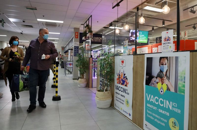 &copy; Reuters. FILE PHOTO: Shoppers, wearing protective face masks, walk past posters for a coronavirus disease (COVID-19) vaccination centre installed inside a supermarket in Brussels, Belgium, August 30, 2021. REUTERS/Bart Biesemans/File Photo