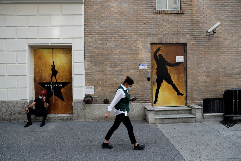© Reuters. امرأة تسير مرتدية كمامة أمام اعلان لعرض مسرحي في برودواي في مانهاتن بنيويورك يوم الثلاثاء. تصوير:رويترز.