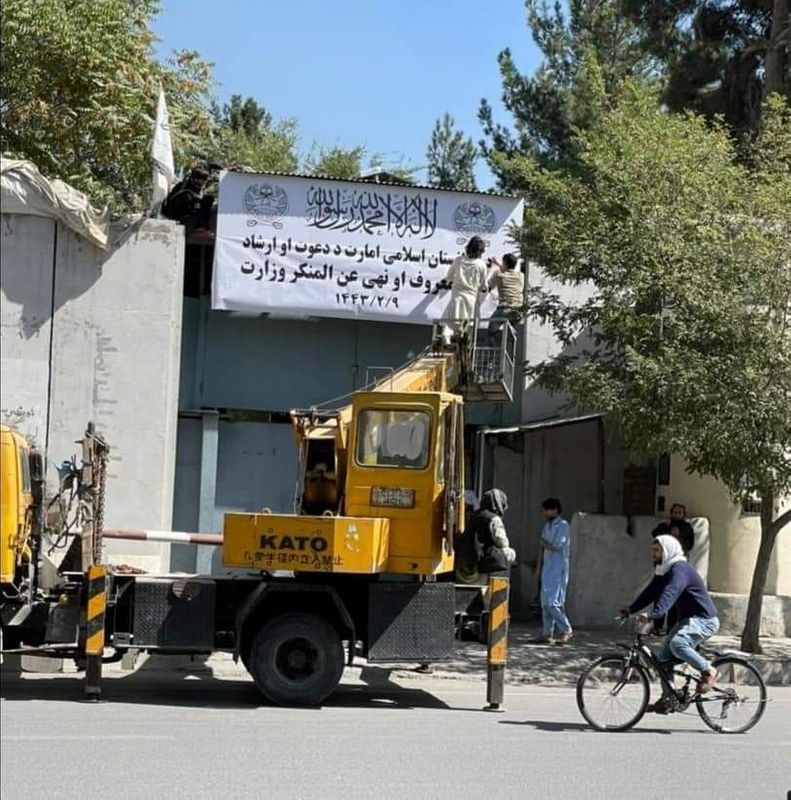 &copy; Reuters. Personas en una grúa mecánica se ocupan de un cartel blanco en el exterior de un edificio en el que se puede leer "Emirato Islámico de Afganistán" y "Ministerios de la oración y la guía y de la Promoción de la Virtud y la Prevención del Vicio" en 