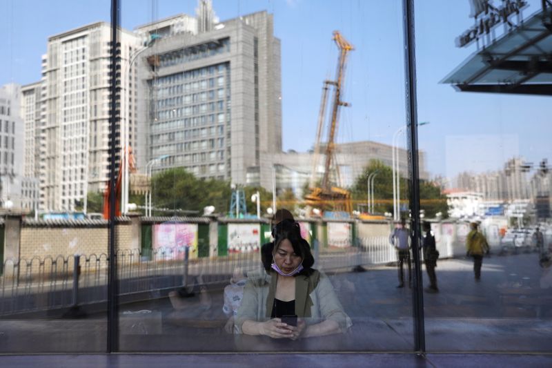 &copy; Reuters. FILE PHOTO: A woman uses a mobile phone inside a cafe as a crane next to buildings is reflected on a glass window, in Tianjin, China September 7, 2021. REUTERS/Tingshu Wang