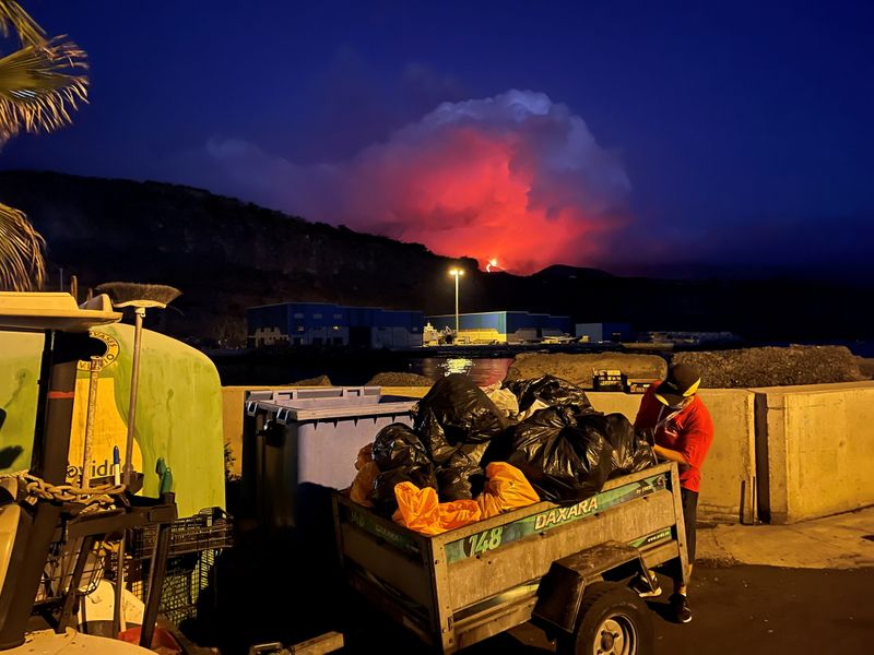 &copy; Reuters. A garbage collector works as lava and smoke rise from an erupting volcano in the Cumbre Vieja park at Tazacorte, on the Canary Island of La Palma, Spain September 25, 2021. REUTERS/Marco Trujillo