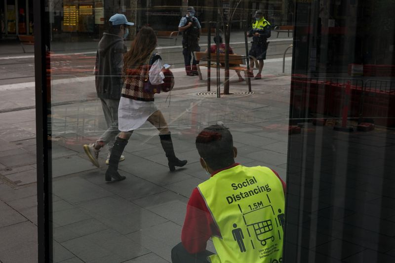 &copy; Reuters. FILE PHOTO: A grocery store employee wearing a vest with social distancing guidelines printed on the back looks on, as police officers check a man in the city centre during a lockdown to curb the spread of a coronavirus disease (COVID-19) outbreak in Sydn