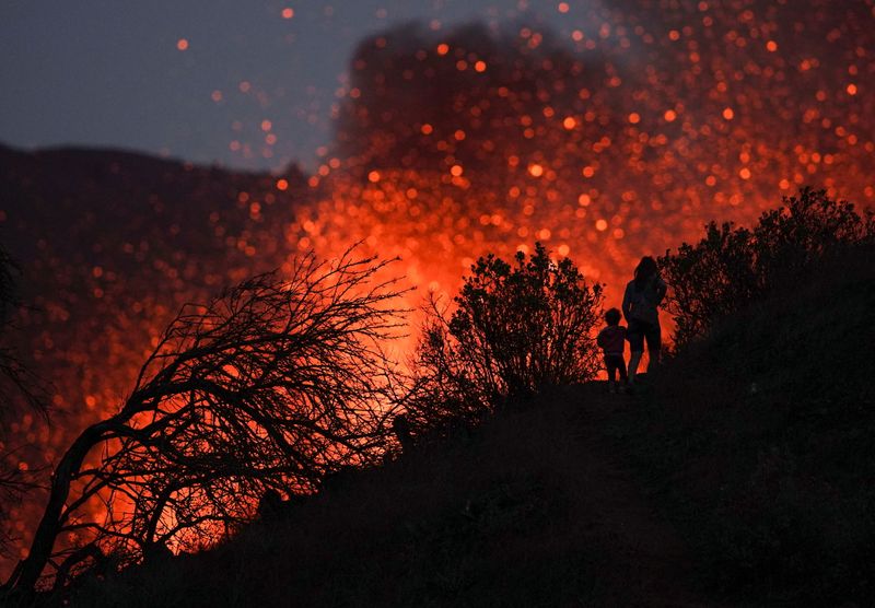 © Reuters. A woman climbs a hill with a child to see the Cumbre Vieja volcano as it continues to erupt in Tacande de Arriba on the Canary Island of La Palma, Spain, October 2, 2021. REUTERS/Juan Medina