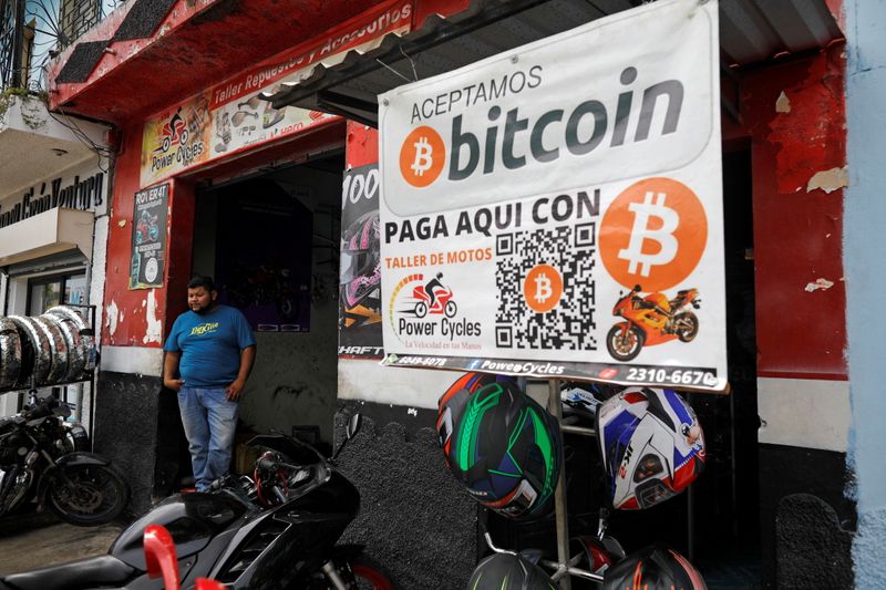 &copy; Reuters. FILE PHOTO: A man stand next to a sign reading "Bitcoin accepted here", outside a moto reapair shop where the cryptocurrency is accepted as a payment method, in Aguilares, El Salvador October 6, 2021. Picture taken October 6, 2021. REUTERS/Jose Cabezas/Fi