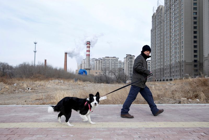 &copy; Reuters. FOTO DE ARCHIVO: Un hombre pasea a su perro frente a un bloque de apartamentos recién construido y una central de carbón en Harbin, en la provincia de Heilongjiang, China, el 26 de noviembre de 2019. REUTERS/Jason Lee