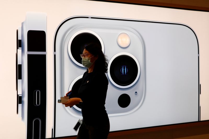 © Reuters. FILE PHOTO: An Apple employee wearing a face mask walks past an image of an iPhone 13 Pro at an Apple Store on the day the new Apple iPhone 13 series goes on sale, in Beijing, China, September 24, 2021. REUTERS/Carlos Garcia Rawlins/File Photo