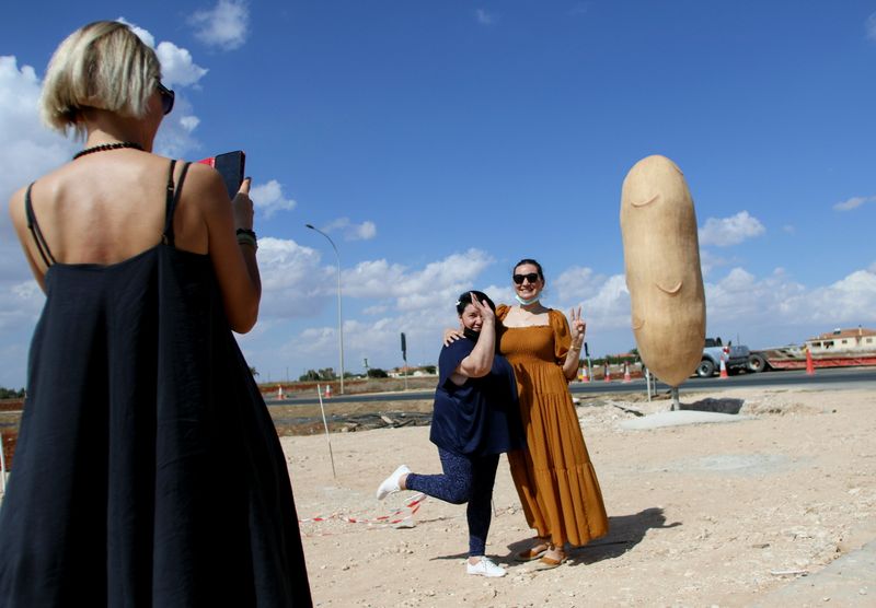 &copy; Reuters. Foto de dos mujeres posando frente a una estatua de una papa en la localidad chipriota de Xylophagou 
Oct 14, 2021. REUTERS/Yiannis Kourtoglou