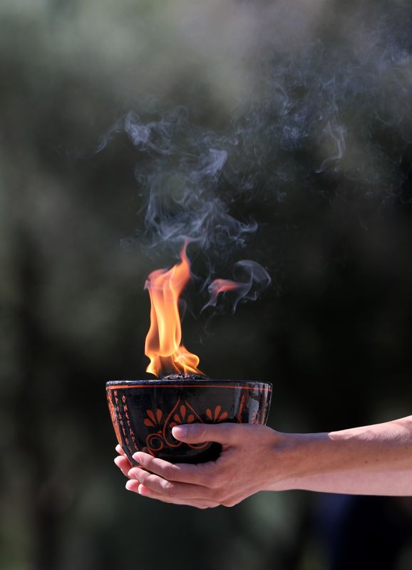 © Reuters. أحد المشاركين في مراسم إيقاد شعلة ألعاب بكين الشتوية في أولمبيا القديمة باليونان يحمل مرجلا تتصاعد منه ألسنة اللهب يوم الاثنين. تصوير:رويترز.