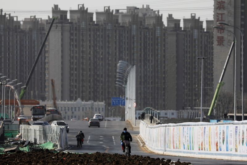 © Reuters. FILE PHOTO: A man rides a bicycle next to a construction site near residential buildings in Beijing, China, January 13, 2021.  REUTERS/Tingshu Wang/File Photo