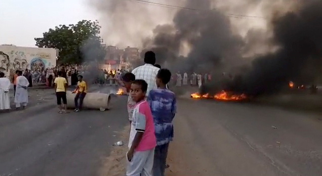 &copy; Reuters. Alcune persone si affollano nelle strade di Kartoum, dove imperversano fiamme e fumo, mentre vengono riportate notizie di un possibile colpo di Stato. Sudan, 25 ottobre 2021. Fotogramma da video diffuso sui social RASD SUDAN NETWORK via REUTERS
