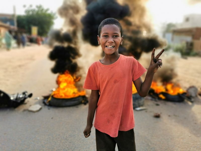 © Reuters. صبي يشير بعلامة النصر أمام اطارات محترقة في الخرطوم يوم الاثنين بعد الانقلاب العسكري. تصوير: الطيب صديق-رويترز.