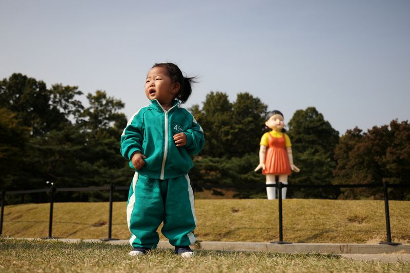 &copy; Reuters. Una niña vestida con un disfraz de la serie de Netflix "El juego del calamar" posa para fotografías frente a una muñeca gigante llamada "Younghee" de la serie, en instalación en un parque en Seúl, Corea del Sur, 26 octubre 2021.
REUTERS/Kim Hong-Ji  
