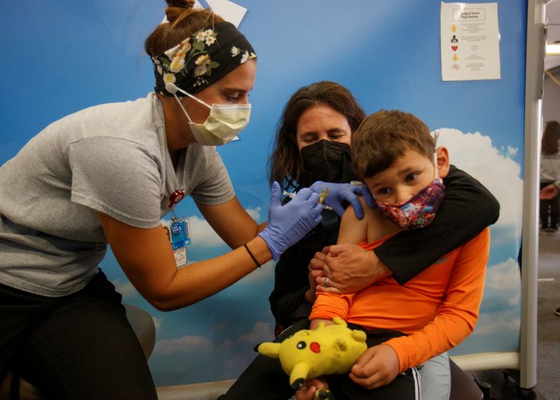 © Reuters. Five year-old Renan Rojas sits on his mom, Daniela Cantano's lap, as he receives the Pfizer-BioNTech coronavirus vaccine from registered nurse Jillian at Rady's Children's hospital vaccination clinic in San Diego, California, U.S., November 3, 2021.  REUTERS/Mike Blake