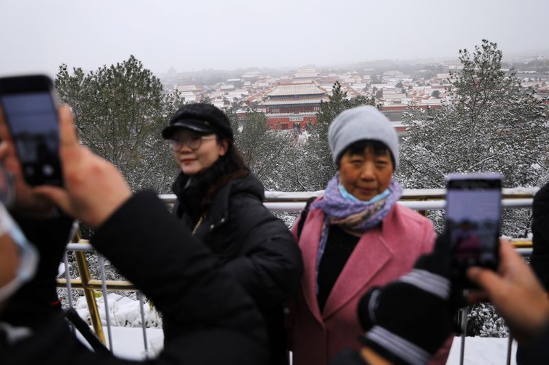 &copy; Reuters. Tourists pose for pictures amid snowfall on a peak overlooking the Forbidden City at Jingshan Park, in Beijing, China November 7, 2021. REUTERS/Tingshu Wang