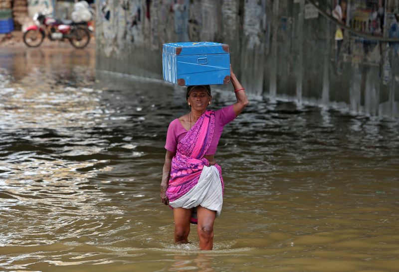 © Reuters. امرأة تحمل صندوقا على رأسها وتسير عبر مياه الفيضانات في نفق عقب  سقوط أمطار غزيرة على تشيناي يوم 3 نوفمبر تشرين الثاني 2021. تصوير:رويترز.