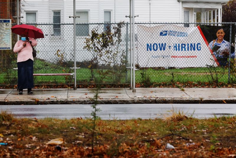 &copy; Reuters. FILE PHOTO: A woman waits for a bus next to a "Now Hiring" sign from the United States Postal Service in Boston, Massachusetts, U.S., October 30, 2021.   REUTERS/Brian Snyder
