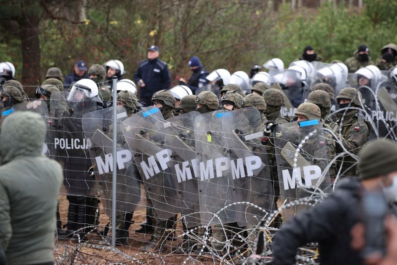 &copy; Reuters. Agentes polacos de la ley y guardias fronterizos junto a una valla de alambre de espino mientras cientos de migrantes se reúnen en la frontera bielorrusa-polaca en un intento de cruzarla en la región de Grodno, Bielorrusia, 8 de noviembre de 2021. REUTE