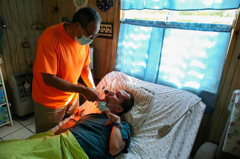 © Reuters. Abraham Rivera Berrios gives a glass of water to his son Emanuel Rivera Fuentes, 35, who was born severely disabled and needs constant care, at his home, in Toa Alta, Puerto Rico, September 22, 2021. Picture taken September 22, 2021.  REUTERS/Alvin Baez
