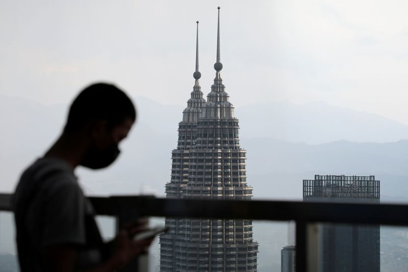 &copy; Reuters. FILE PHOTO: A man wearing a protective mask uses his phone as the Petronas Twin Towers are seen in the background in Kuala Lumpur, Malaysia April 12, 2021. REUTERS/Lim Huey Teng/File Photo