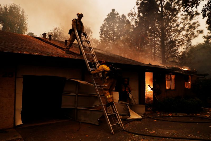 &copy; Reuters. FILE PHOTO: A firefighter climbs a ladder by a burning structure while battling the Camp Fire in Paradise, California, U.S., November 9, 2018. REUTERS/Stephen Lam/File Photo