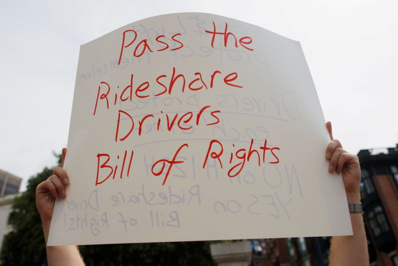 &copy; Reuters. FILE PHOTO: A protestor holds a sign reading “Pass the Rideshare Drivers Bill of Rights” at a demonstration opposing a ballot campaign by companies such has Uber, Lyft and Door Dash to exempt their companies from some labor laws, outside the Massachus